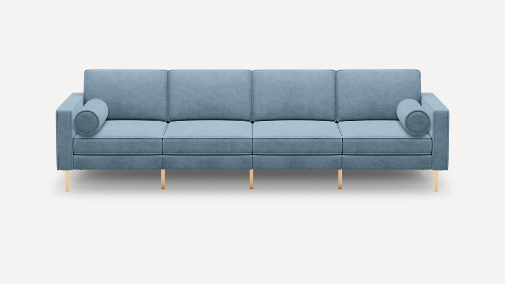 Modern four-seater sofa in light blue fabric with cylindrical bolster pillows and sleek gold metal legs.