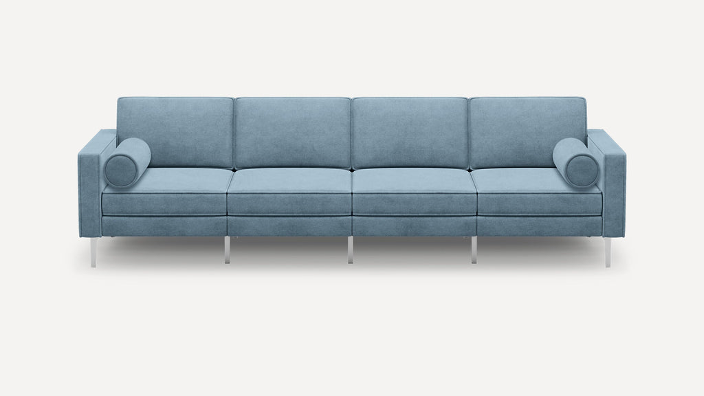 Modern light blue four-seater sofa with rectangular cushions, cylindrical bolster pillows, and slim metallic legs on a white background.