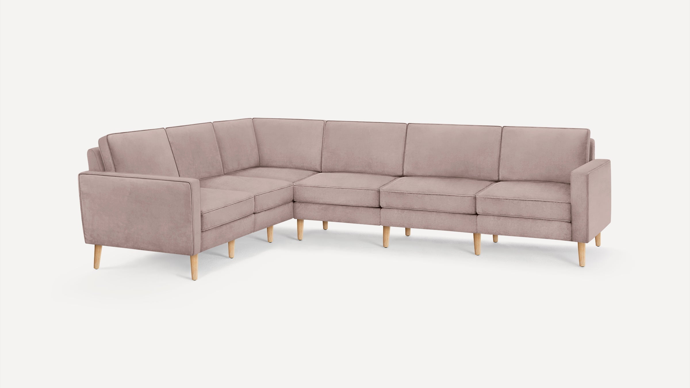 L-shaped sectional sofa with soft pink upholstery and light wooden legs, featuring clean lines and cushioned seats and backs.
