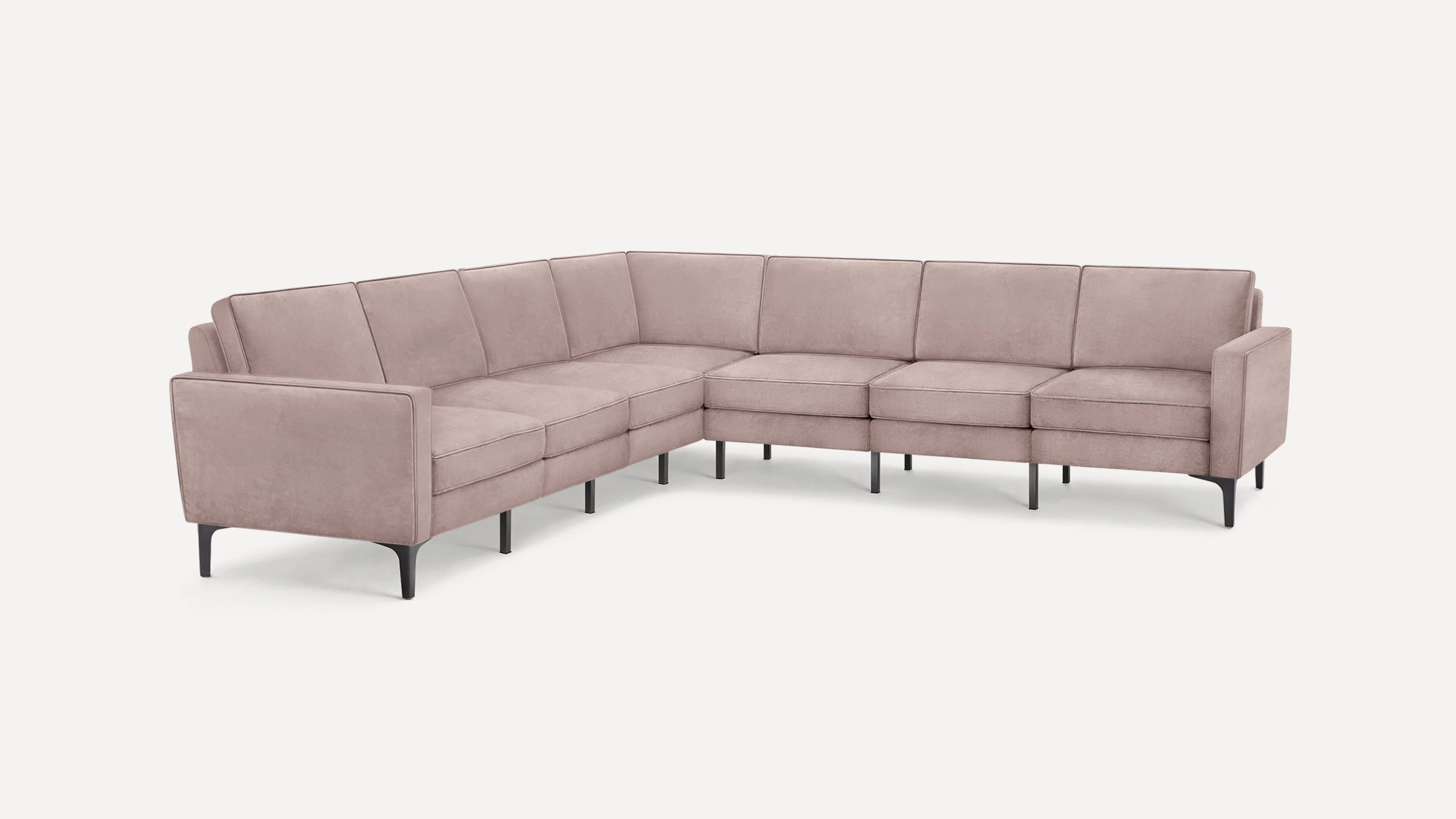 Modern L-shaped sectional sofa in soft pink fabric with slim black legs and clean, boxy design.