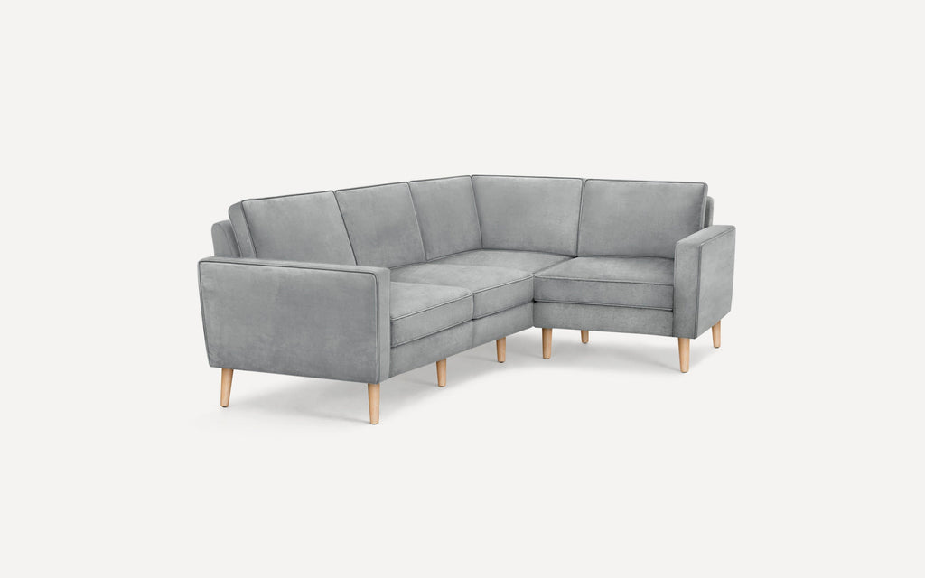 Modern light gray L-shaped sectional sofa with wooden legs and cushioned back and seat on a white background.