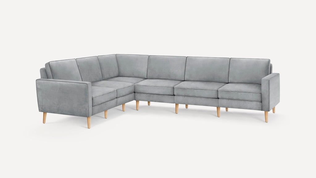 Modern L-shaped sectional sofa in soft gray fabric with sleek lines and light wooden legs on white background.
