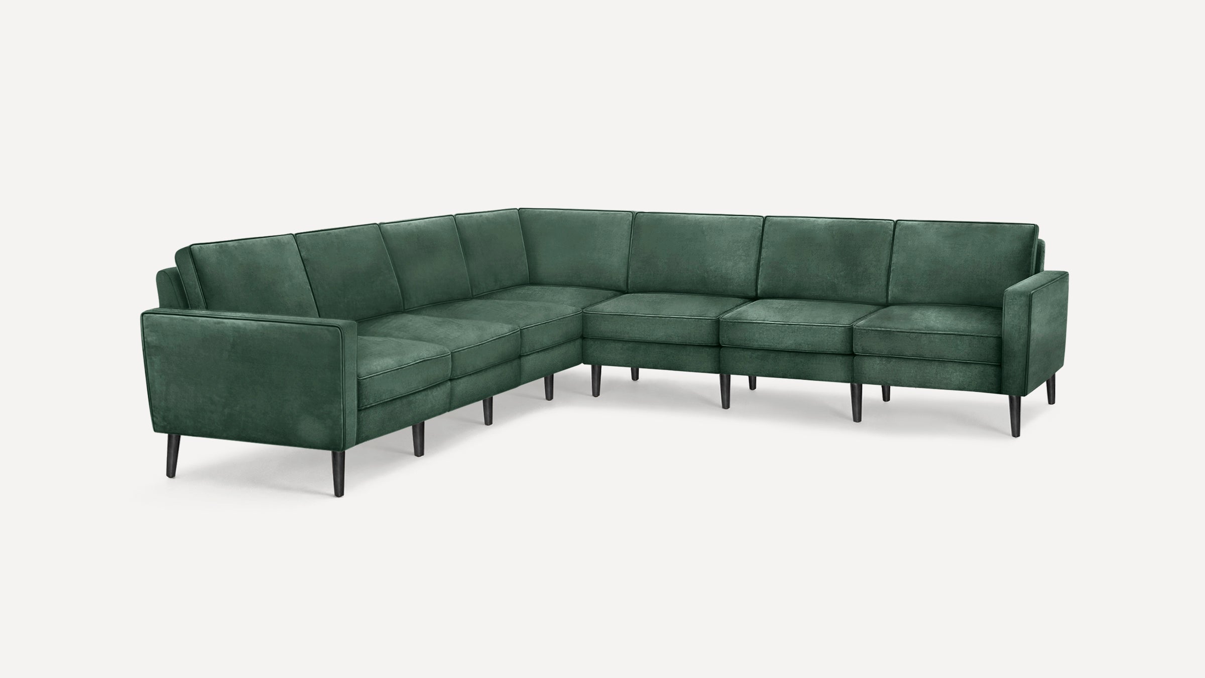 L-shaped sectional sofa upholstered in dark green velvet fabric with thin armrests and tapered black legs on white background.