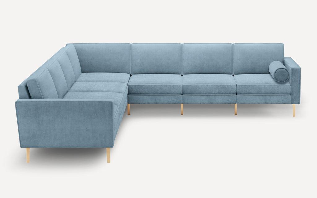 L-shaped modern sectional sofa in light blue fabric with clean lines, cushioned seats, and a cylindrical bolster pillow on one end.