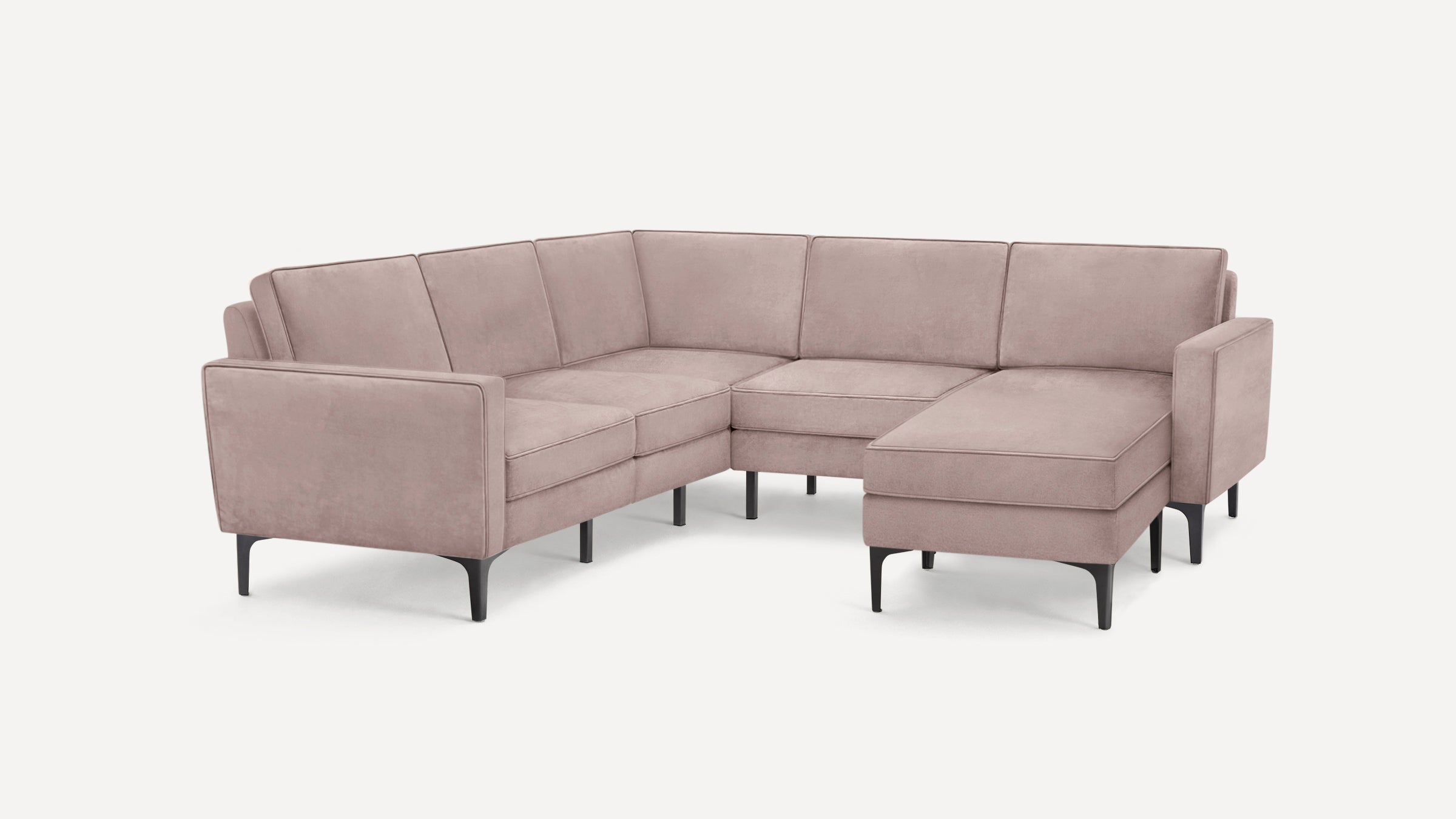 Modern L-shaped sectional sofa with soft dusty pink upholstery and black metal legs, featuring clean lines and a chaise lounge.