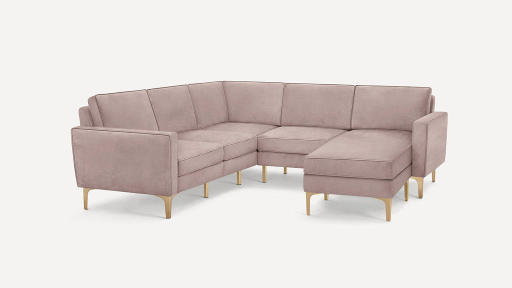 Modern L-shaped sectional sofa in soft dusty pink upholstery with gold metal legs and clean, square armrests.