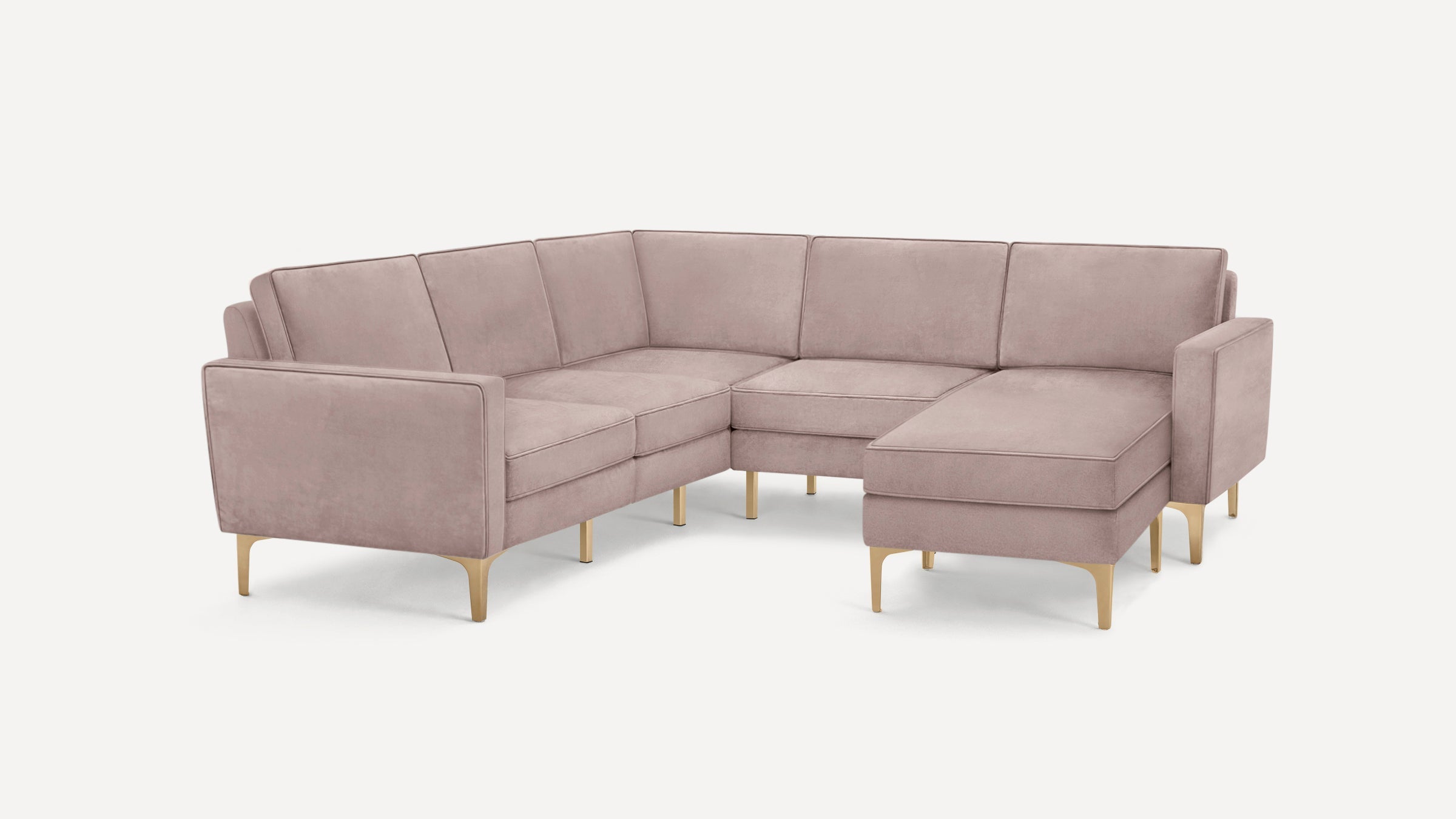Modern L-shaped sectional sofa in soft dusty pink upholstery with gold metal legs and clean, square armrests.