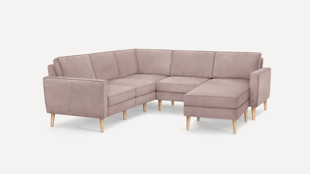 Light mauve L-shaped sectional sofa with straight armrests and wooden legs on white background.