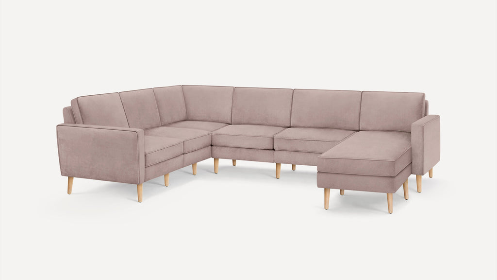 Large L-shaped sectional sofa with light mauve upholstery and wooden legs, featuring clean lines and modern design.