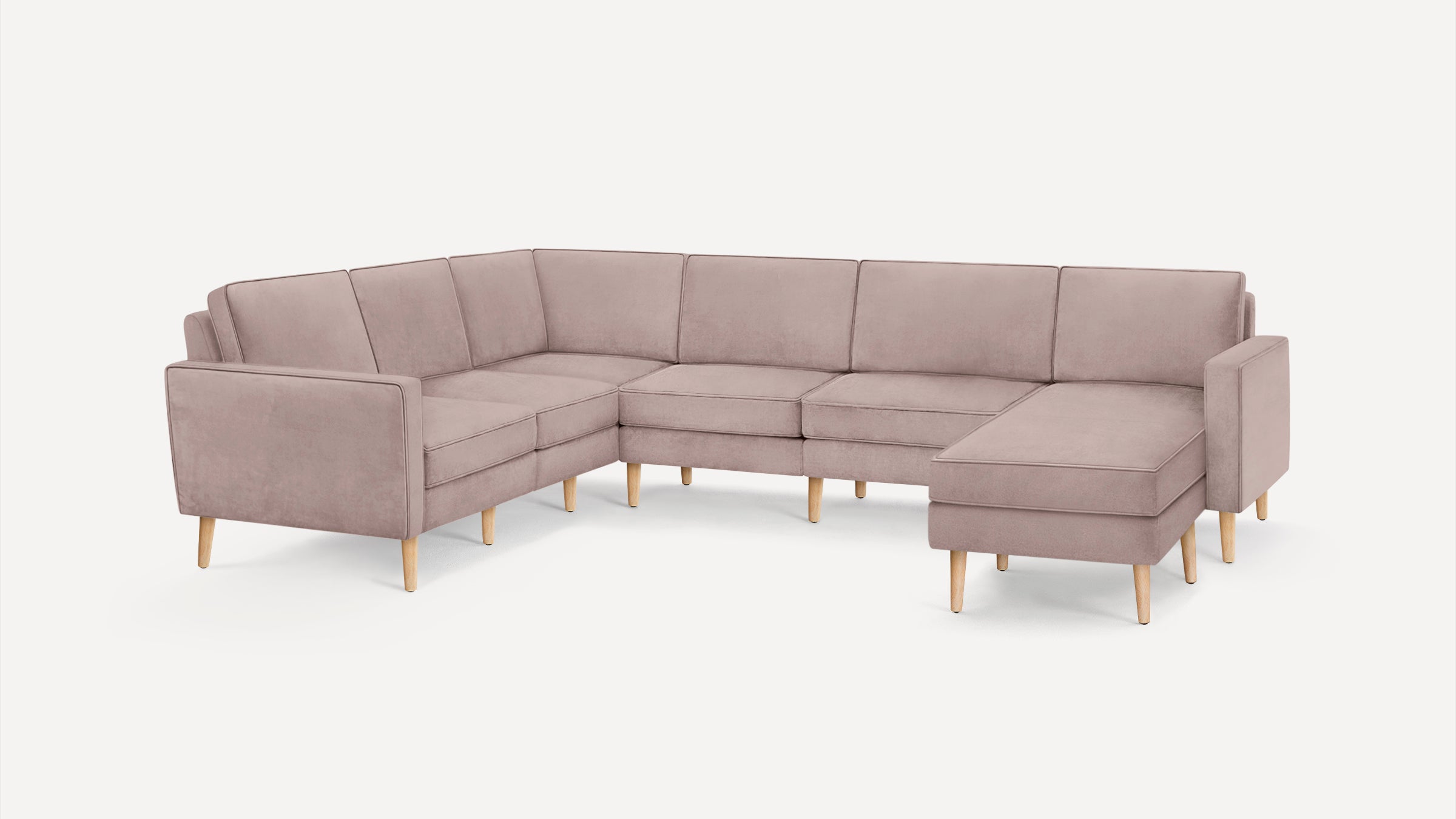 Large L-shaped sectional sofa with light mauve upholstery and wooden legs, featuring clean lines and modern design.