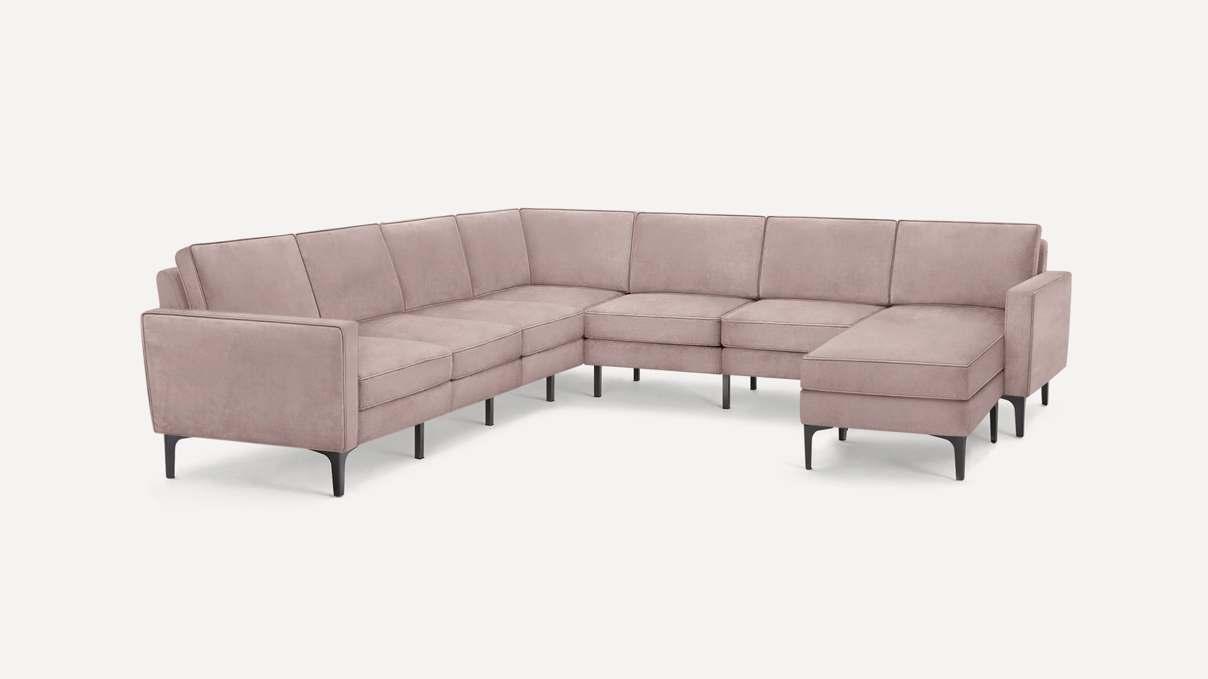 L-shaped sectional sofa in soft pink velvet fabric with black tapered legs and cushioned backrests and seats.
