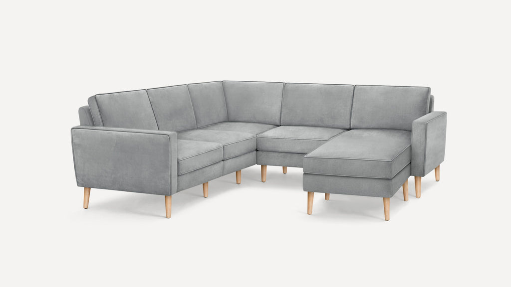 Modern L-shaped sectional sofa in light gray fabric with tapered wooden legs and clean, minimalist design.