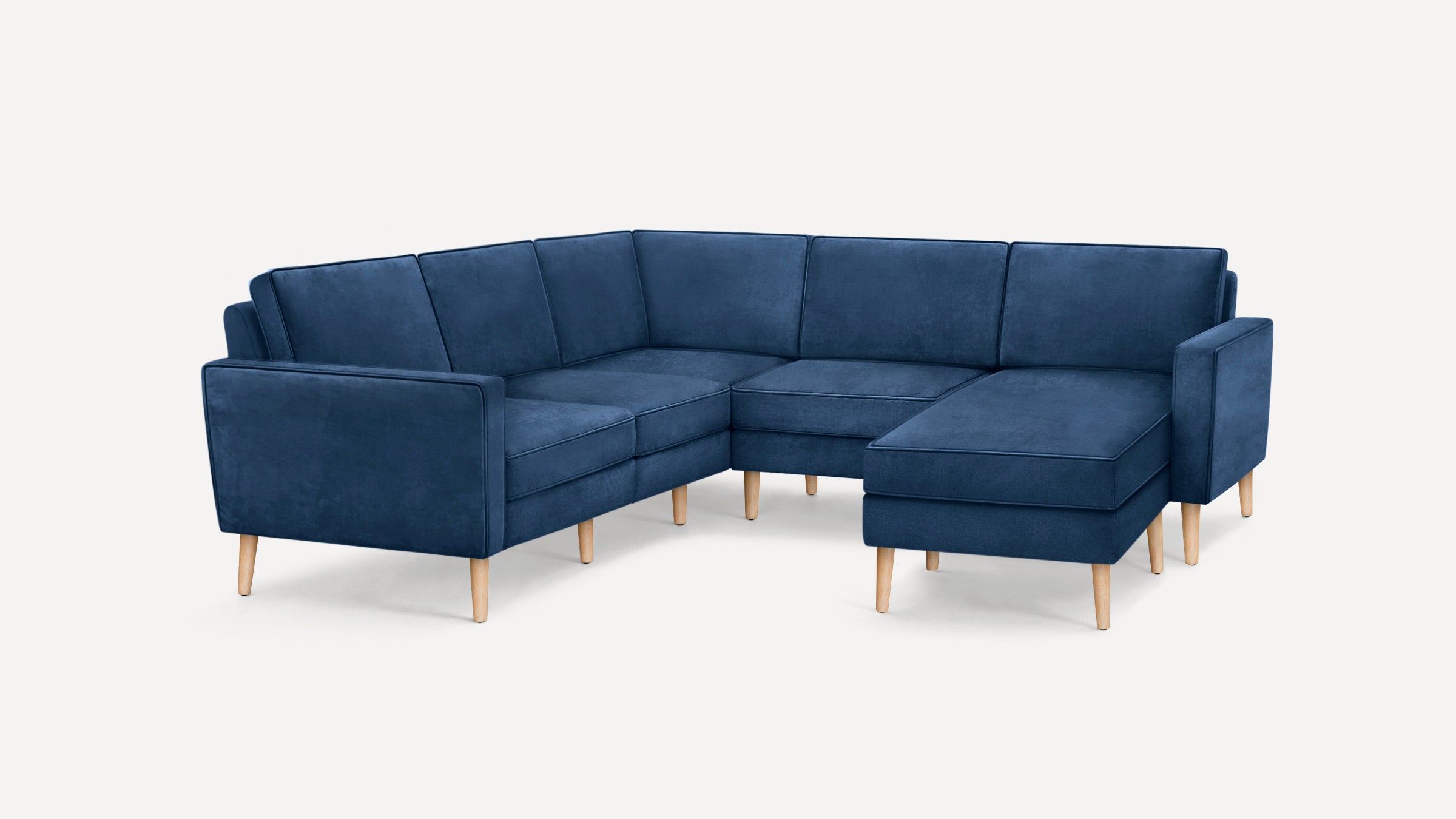 Modern L-shaped sectional sofa in deep blue velvet fabric with wooden tapered legs and clean, straight lines.
