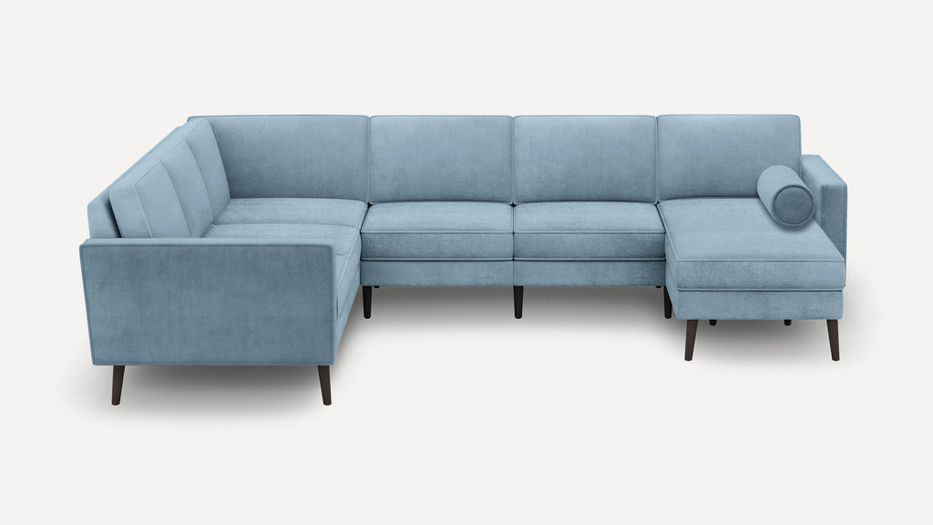 Light blue L-shaped sectional sofa with wooden legs and a cylindrical bolster pillow on the right chaise lounge.