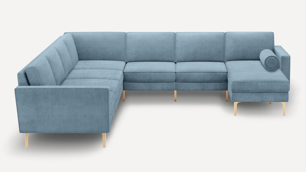 Modern light blue sectional sofa with clean lines, gold metal legs, tufted cushions, and a cylindrical bolster pillow on the right chaise.