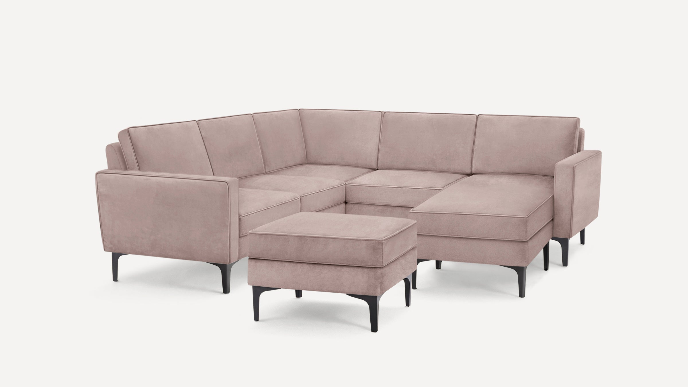 Modern light mauve velvet sectional sofa with black angled legs and matching ottoman on white background.