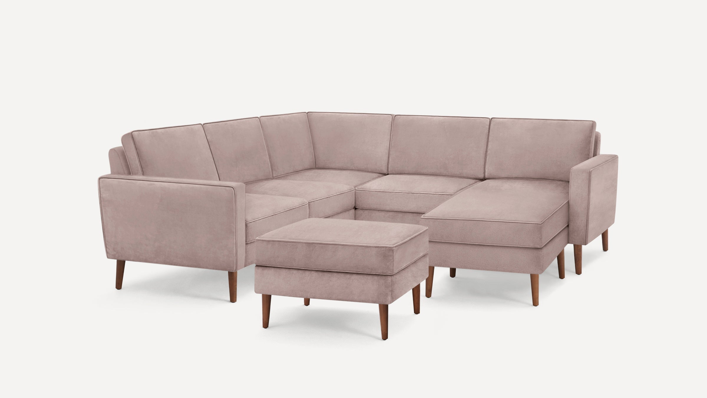 Light mauve velvet upholstered L-shaped sectional sofa with wooden tapered legs and matching ottoman.