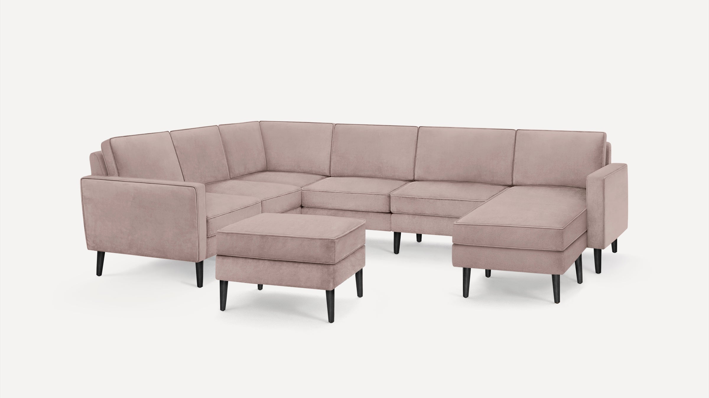 Light pink upholstered sectional sofa with clean lines and black tapered wooden legs, including a matching ottoman.
