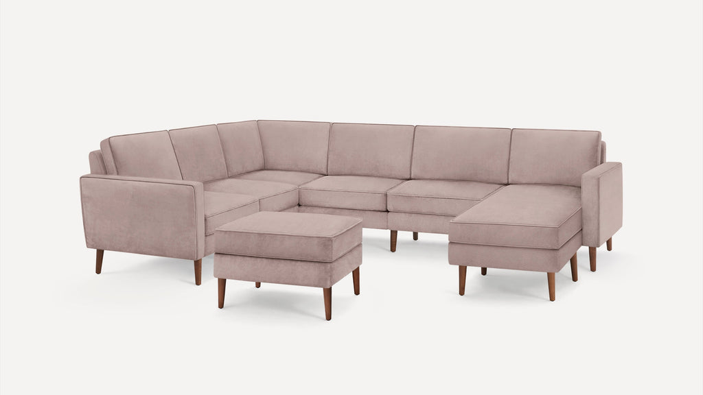 Light pink velvet U-shaped sectional sofa with wooden legs and matching ottoman, modern and minimalist design.