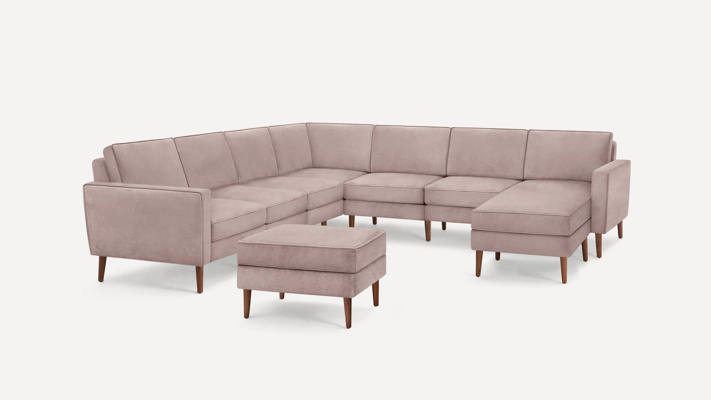 Light mauve L-shaped sectional sofa with wooden legs and matching ottoman, modern and plush design.