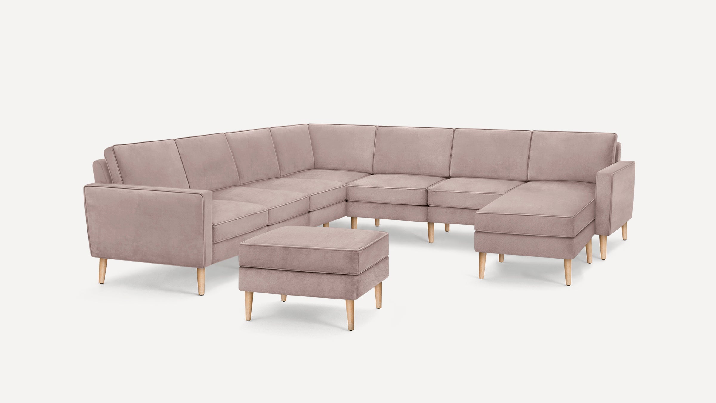 Light mauve velvet L-shaped sectional sofa with wooden legs and matching ottoman, modern and minimalist design.