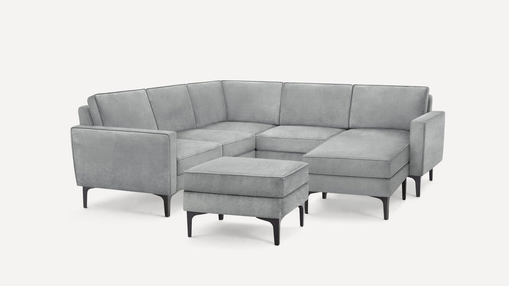 Modern gray upholstered sectional sofa with clean lines, consisting of a corner seat, chaise lounge, and matching ottoman on black legs.
