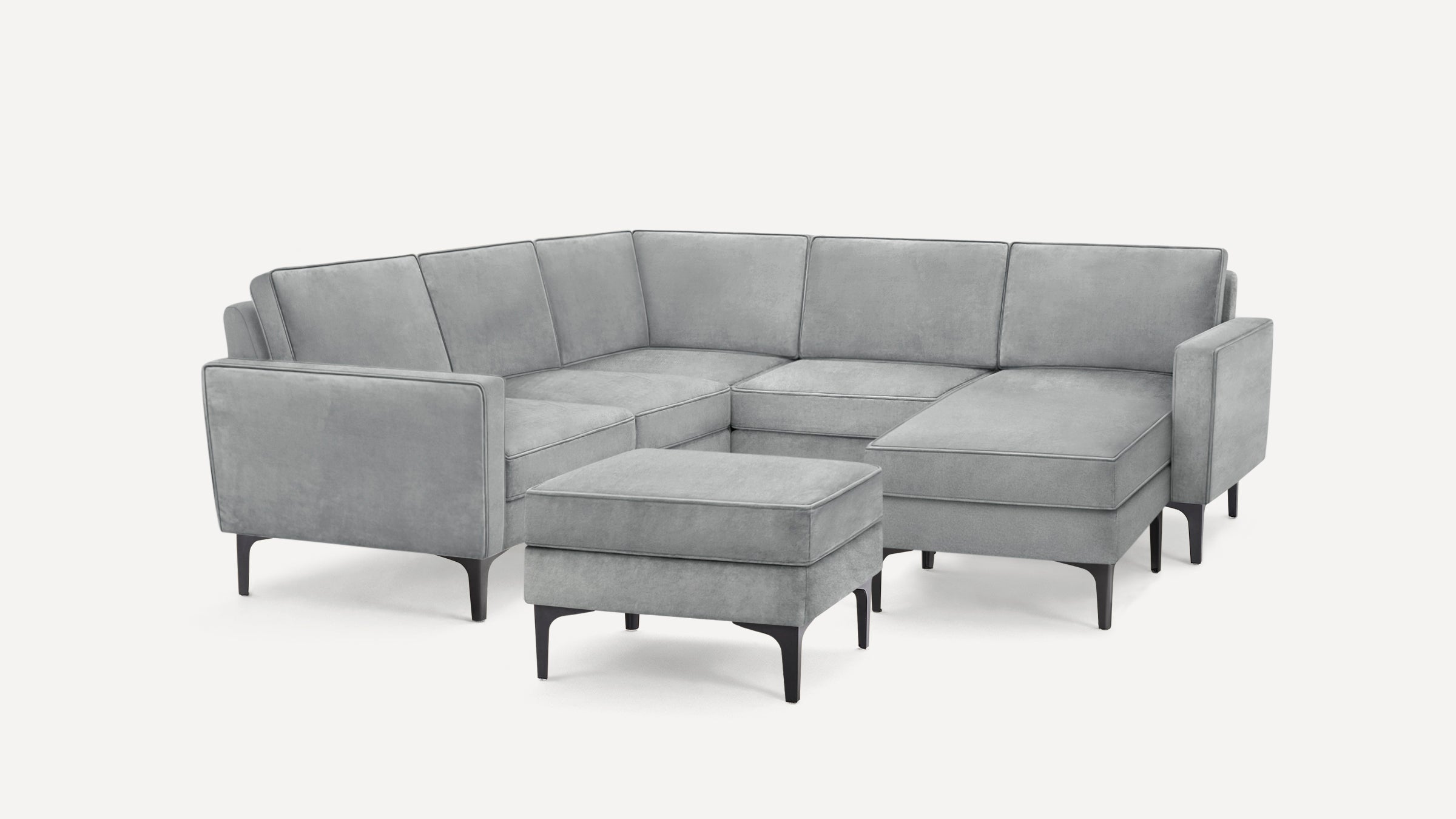 Modern gray upholstered sectional sofa with clean lines, consisting of a corner seat, chaise lounge, and matching ottoman on black legs.
