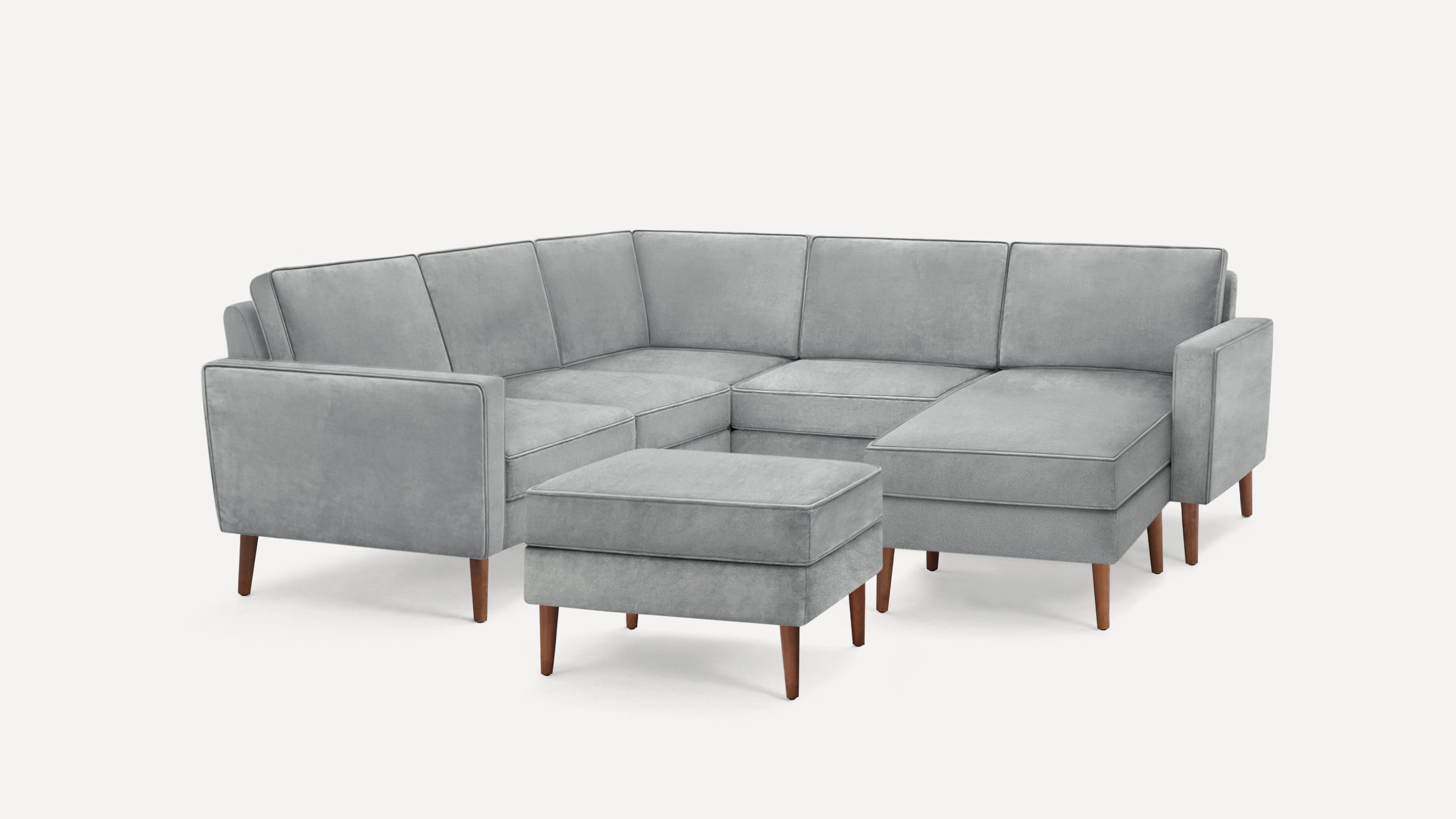Light gray sectional sofa with matching ottoman, sleek wooden legs, and modern, minimalist design on white background.