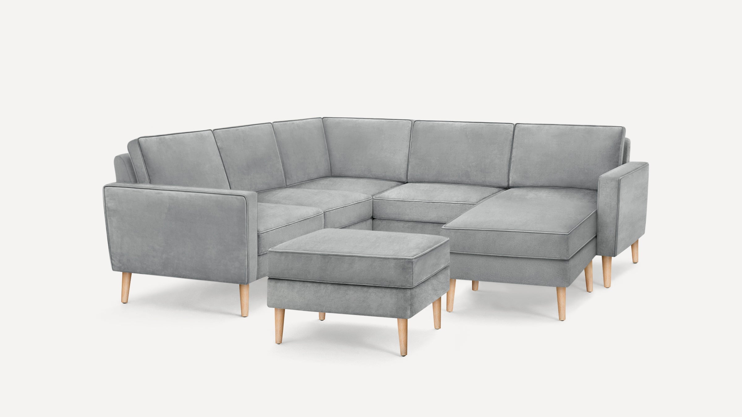 Light gray L-shaped sectional sofa with wooden legs and a matching ottoman on a white background.