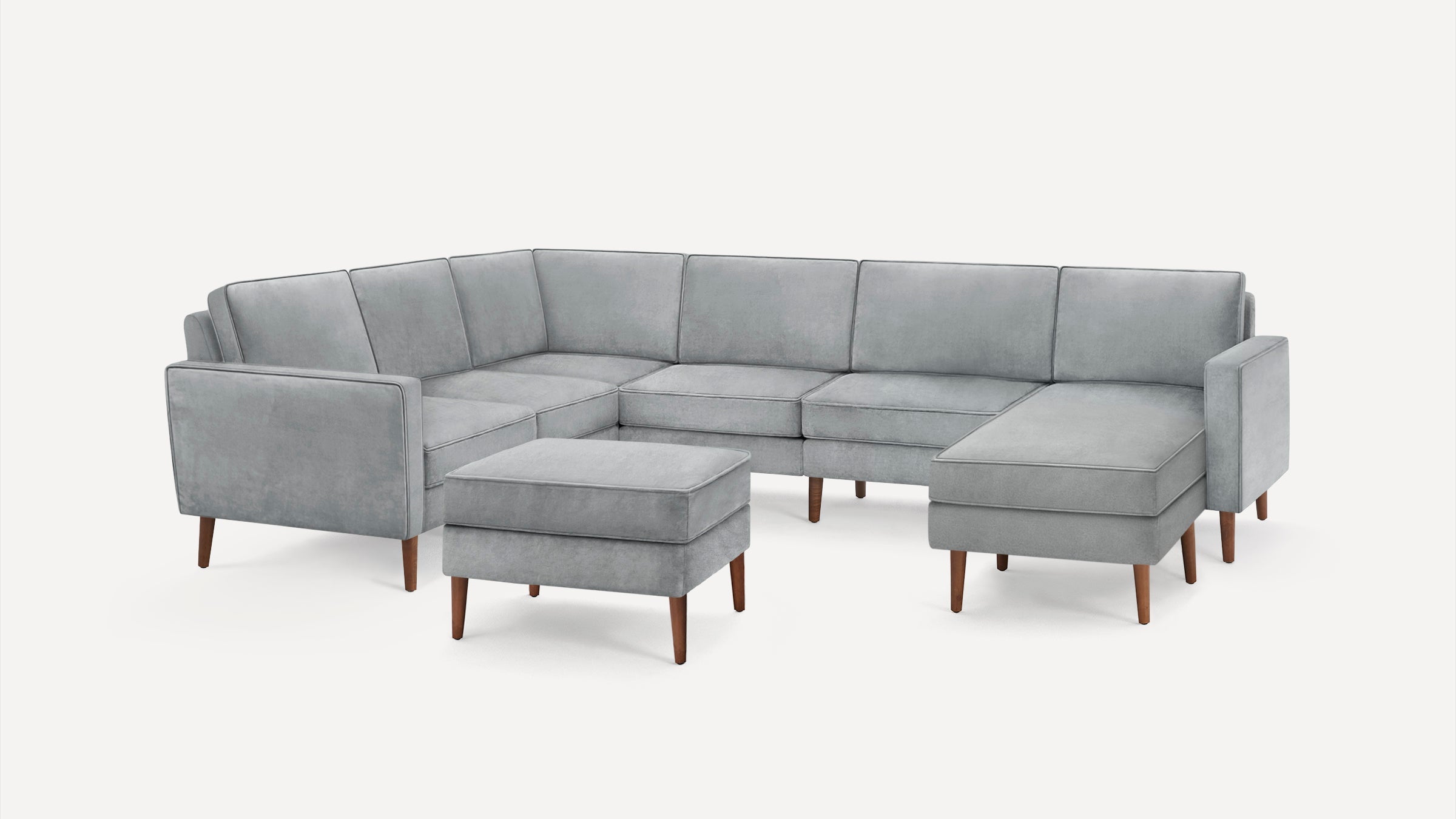 Light grey L-shaped sectional sofa with matching ottoman and wooden legs, minimalist modern design on white background.