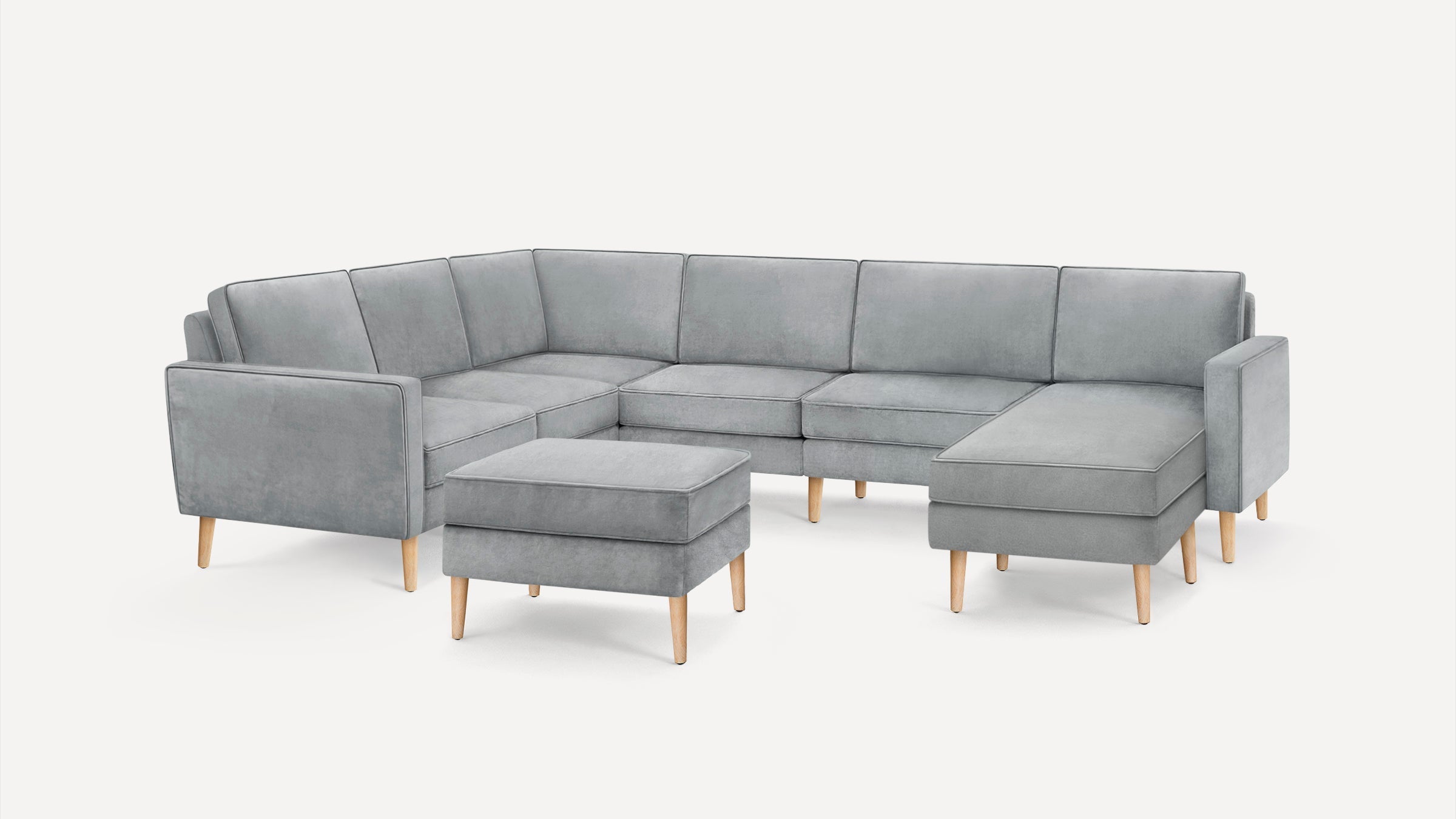 Light gray L-shaped sectional sofa with matching ottoman, featuring wooden legs and clean modern lines on a white background.
