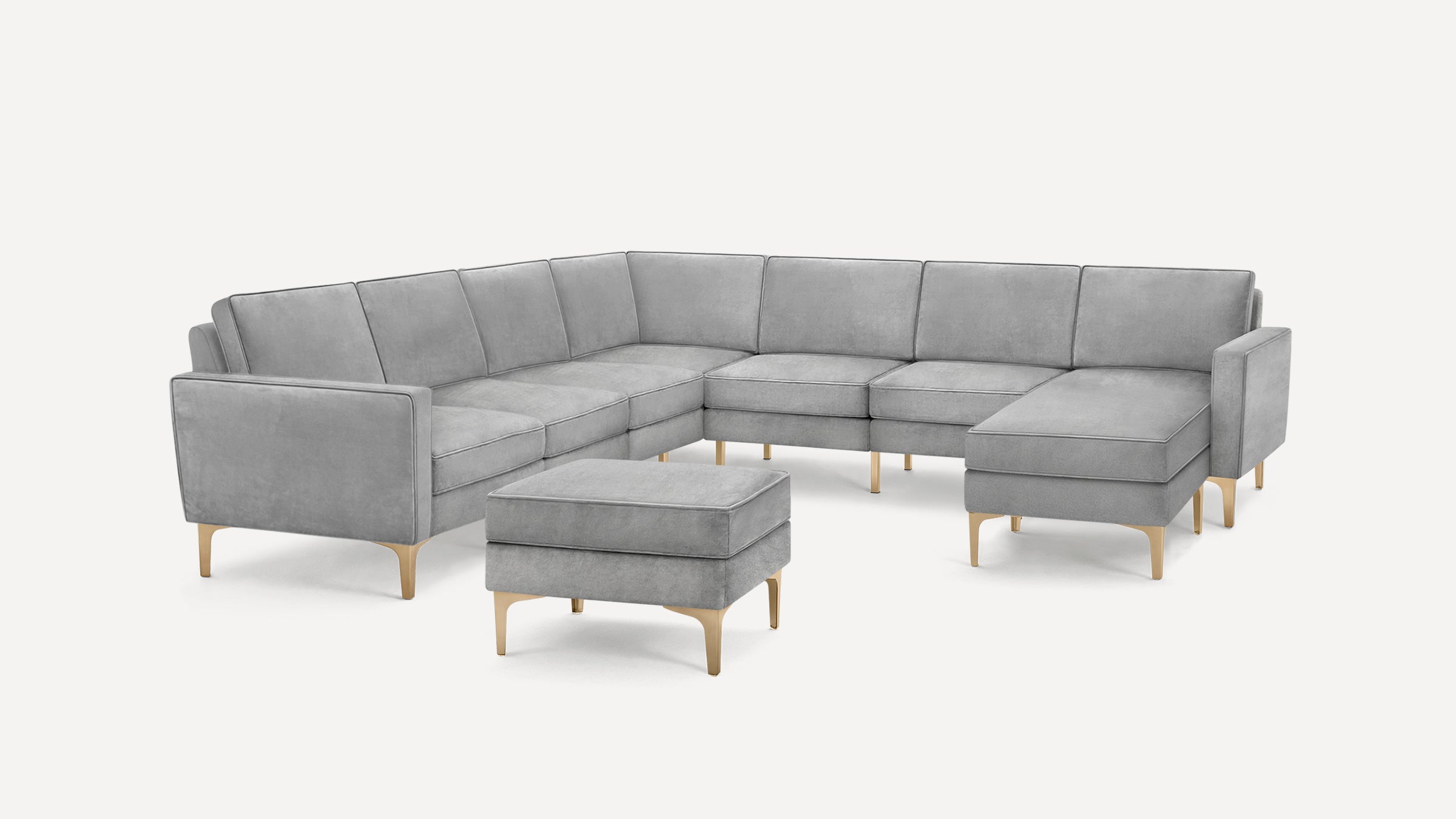 Modern gray L-shaped sectional sofa with gold metal legs and matching ottoman on a white background.