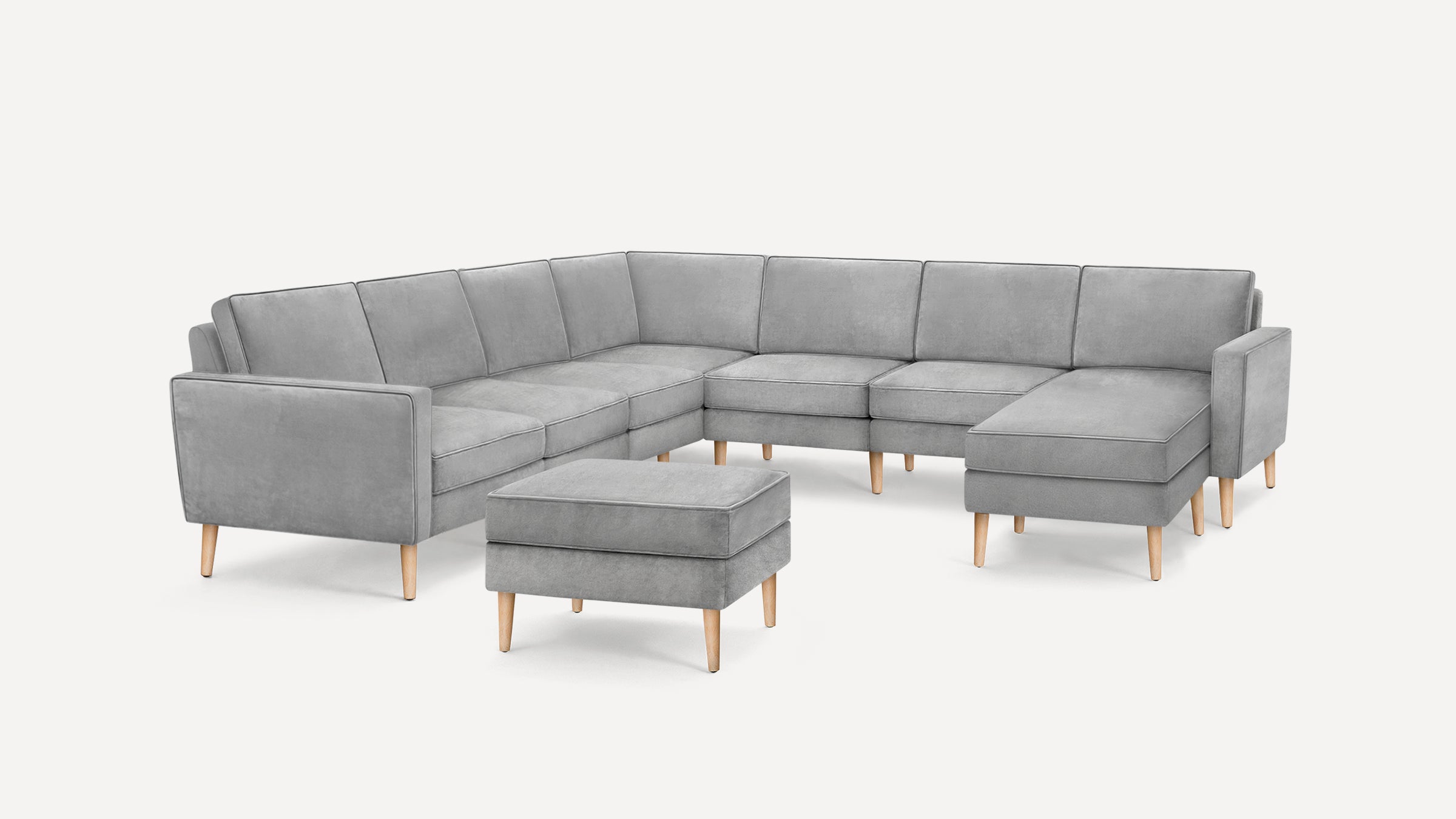 Modern L-shaped gray sectional sofa with clean lines, wooden legs, and a matching cushioned ottoman on a white background.