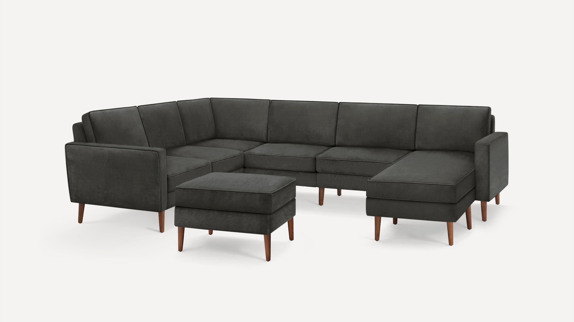 Dark gray L-shaped sectional sofa with wooden legs and matching ottoman on white background.
