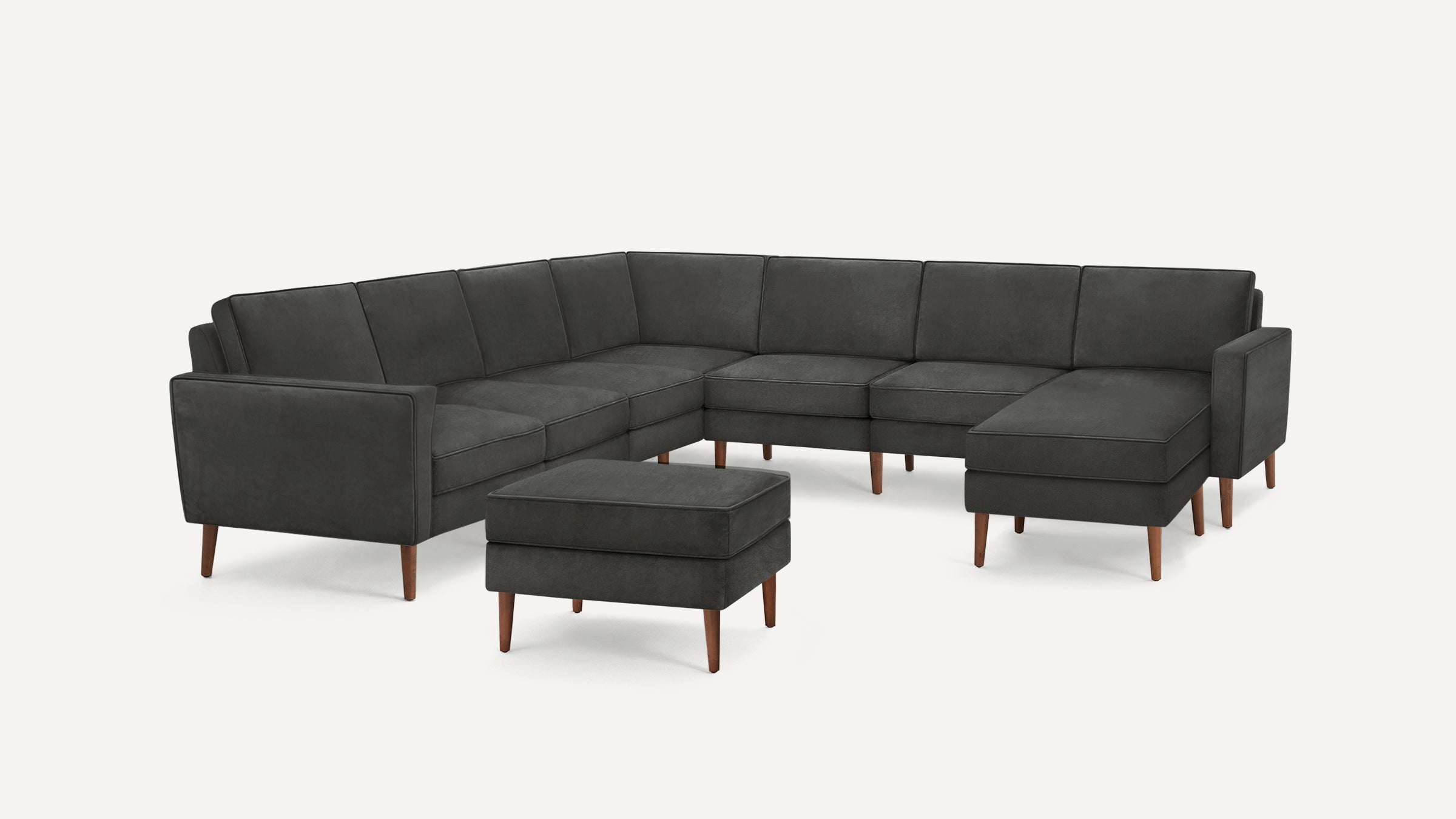 Modern dark gray sectional sofa with wooden legs and a matching ottoman on a white background.