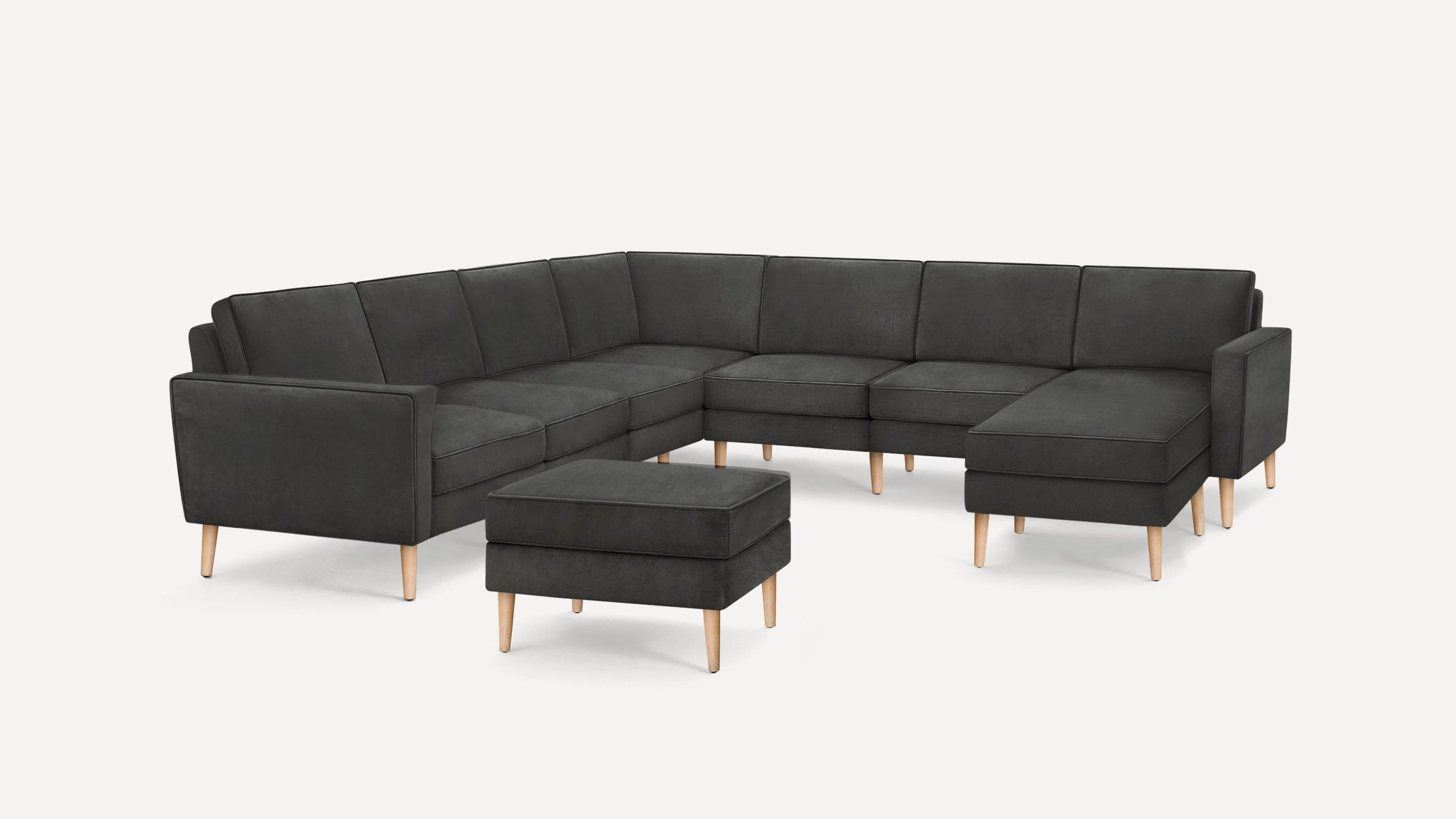 Modern dark gray L-shaped sectional sofa with light wooden legs and matching ottoman on a plain white background.