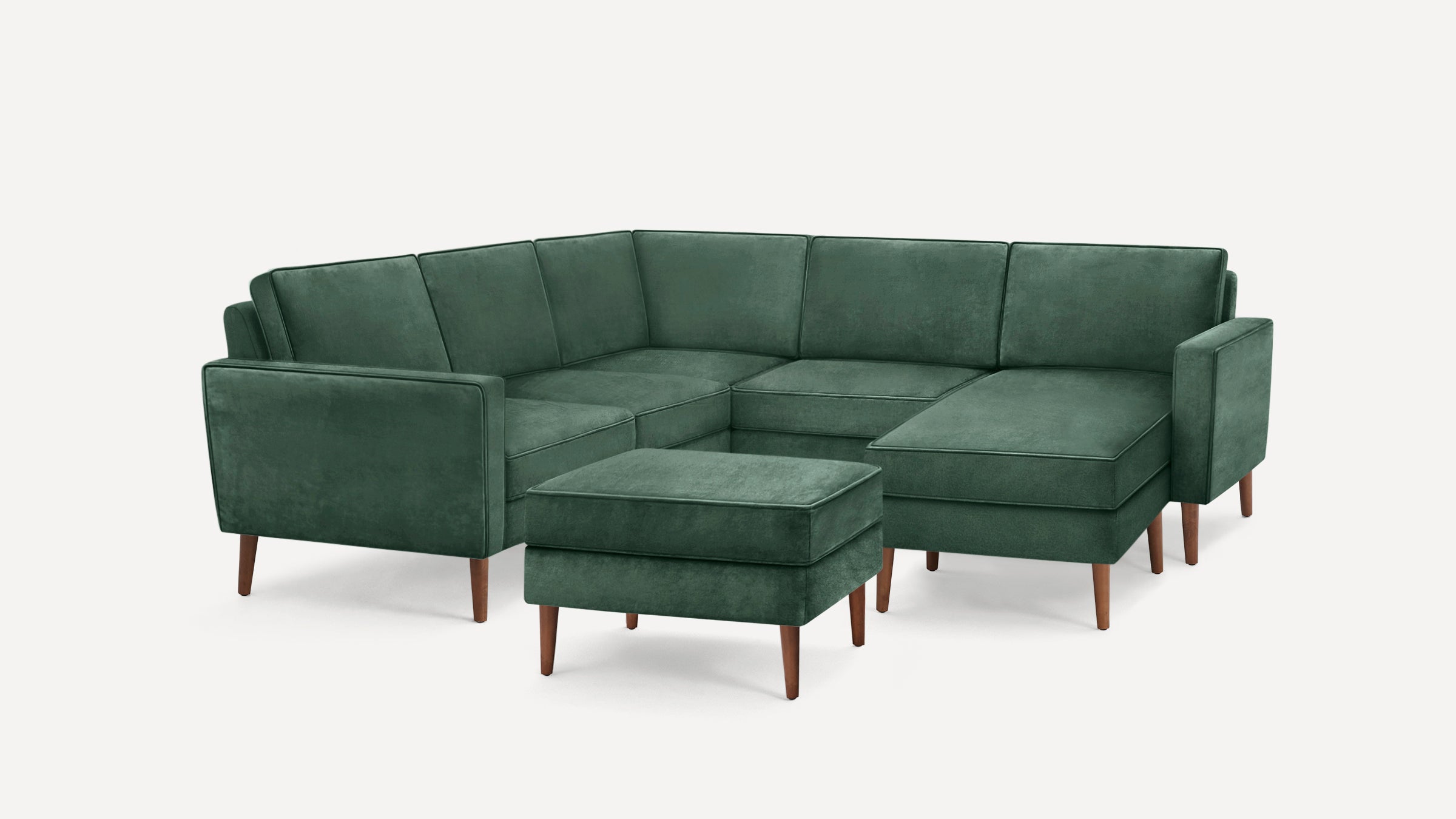 Dark green velvet sectional sofa with wooden legs and a matching ottoman, displayed on a white background.
