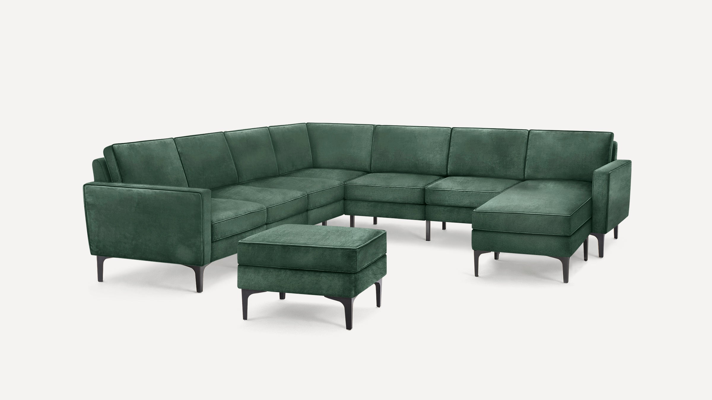 Green velvet L-shaped sectional sofa with matching ottoman, slim dark legs, and clean, modern design.