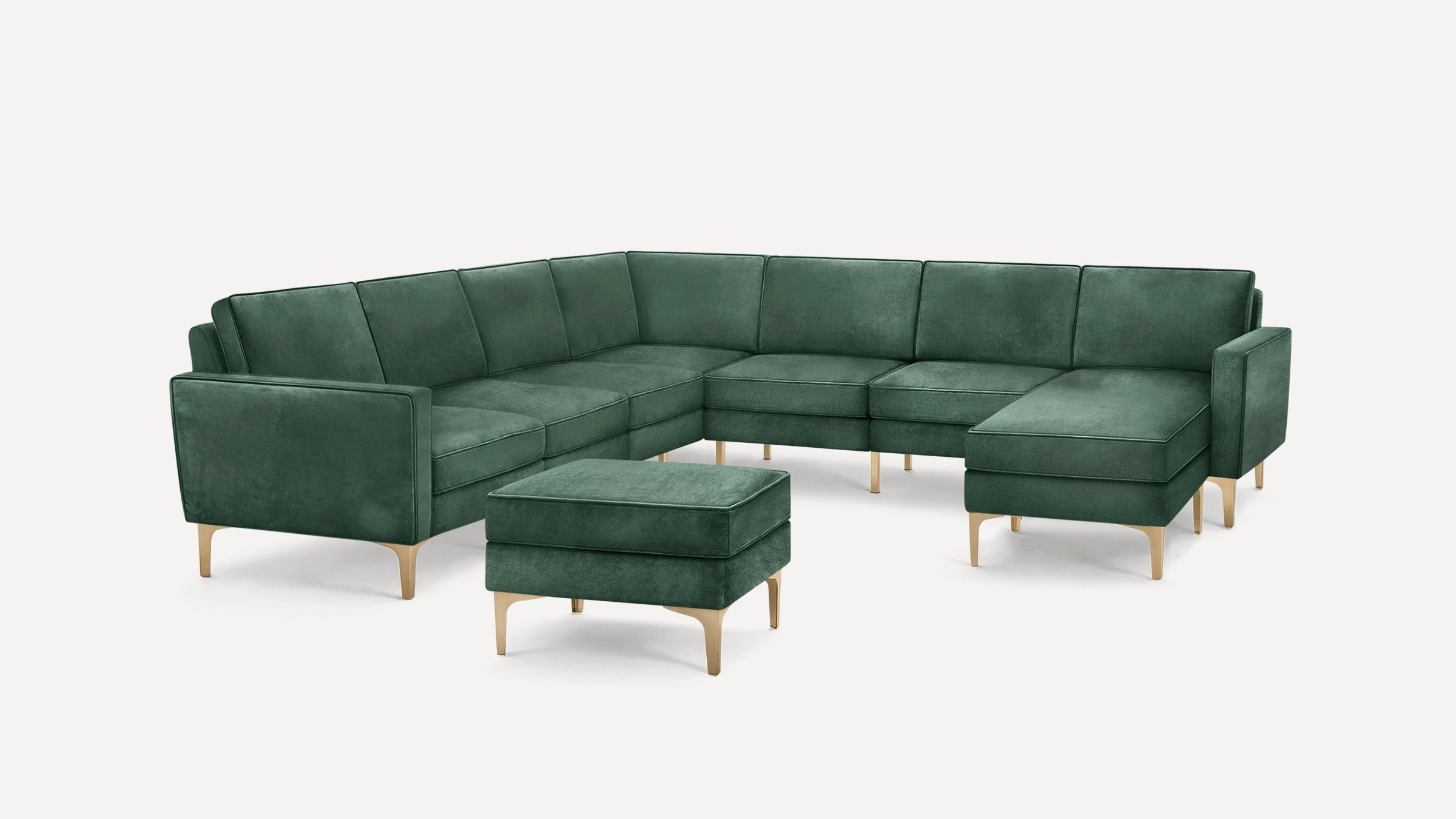 Dark green velvet L-shaped sectional sofa with matching ottoman and light wooden legs on a white background.