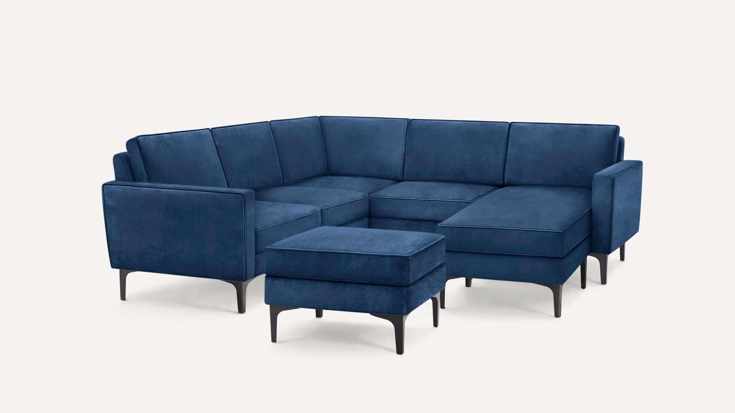 Modern navy blue velvet L-shaped sectional sofa with slim black metal legs and matching ottoman on white background.