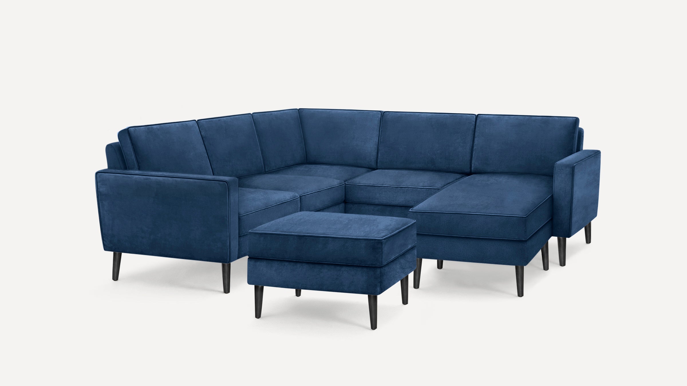 Modern navy blue velvet sectional sofa with matching ottoman, featuring clean lines and slim black wooden legs.