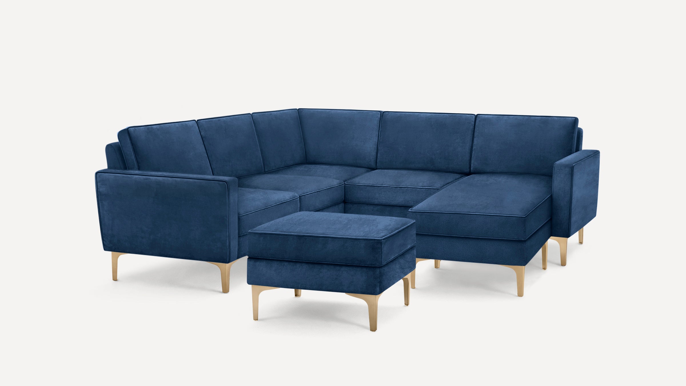 Modern navy blue velvet sectional sofa with gold metal legs and matching ottoman on white background.