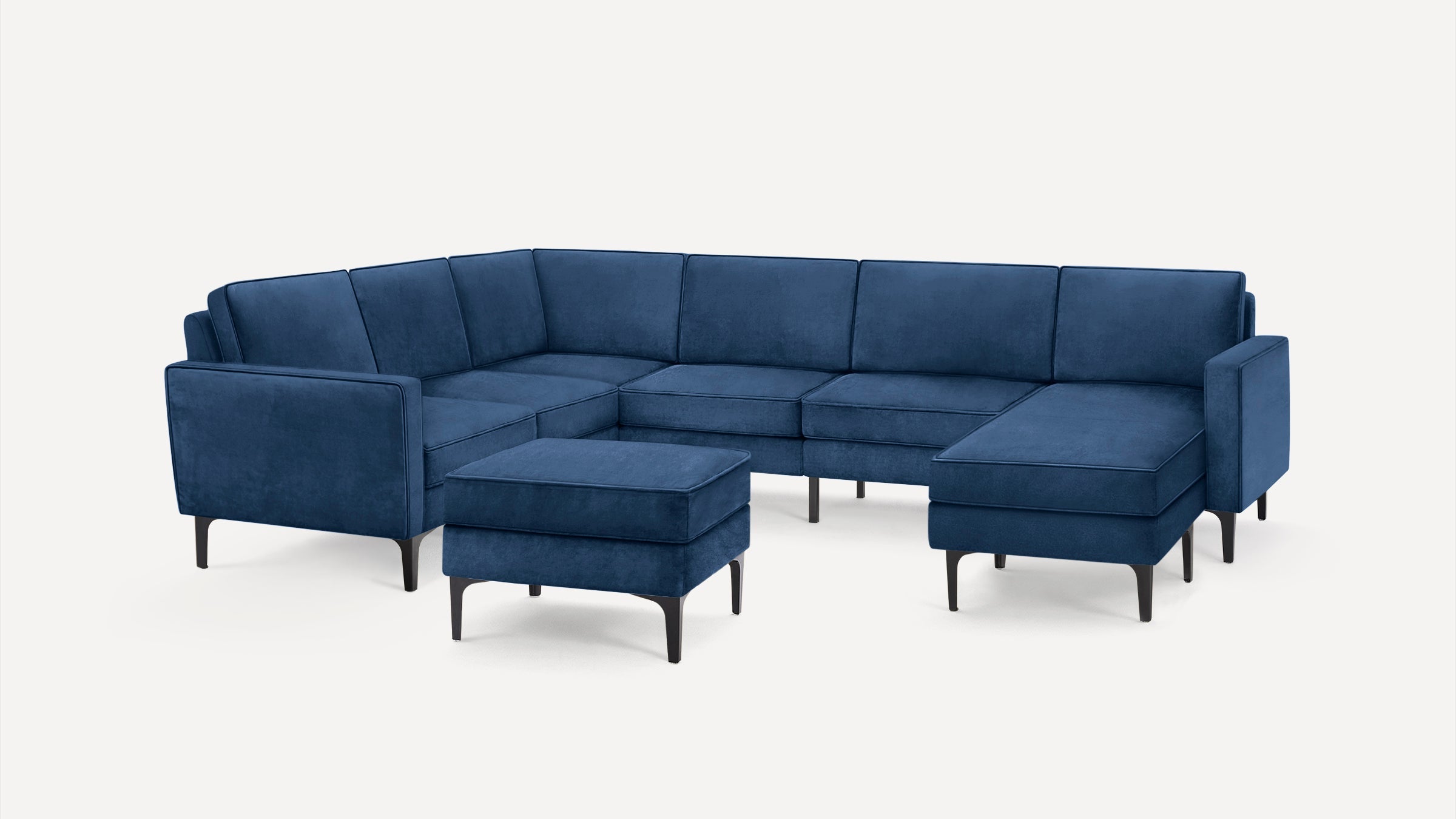 Modern sectional sofa in deep blue velvet with clean lines, black tapered legs, and a matching ottoman.