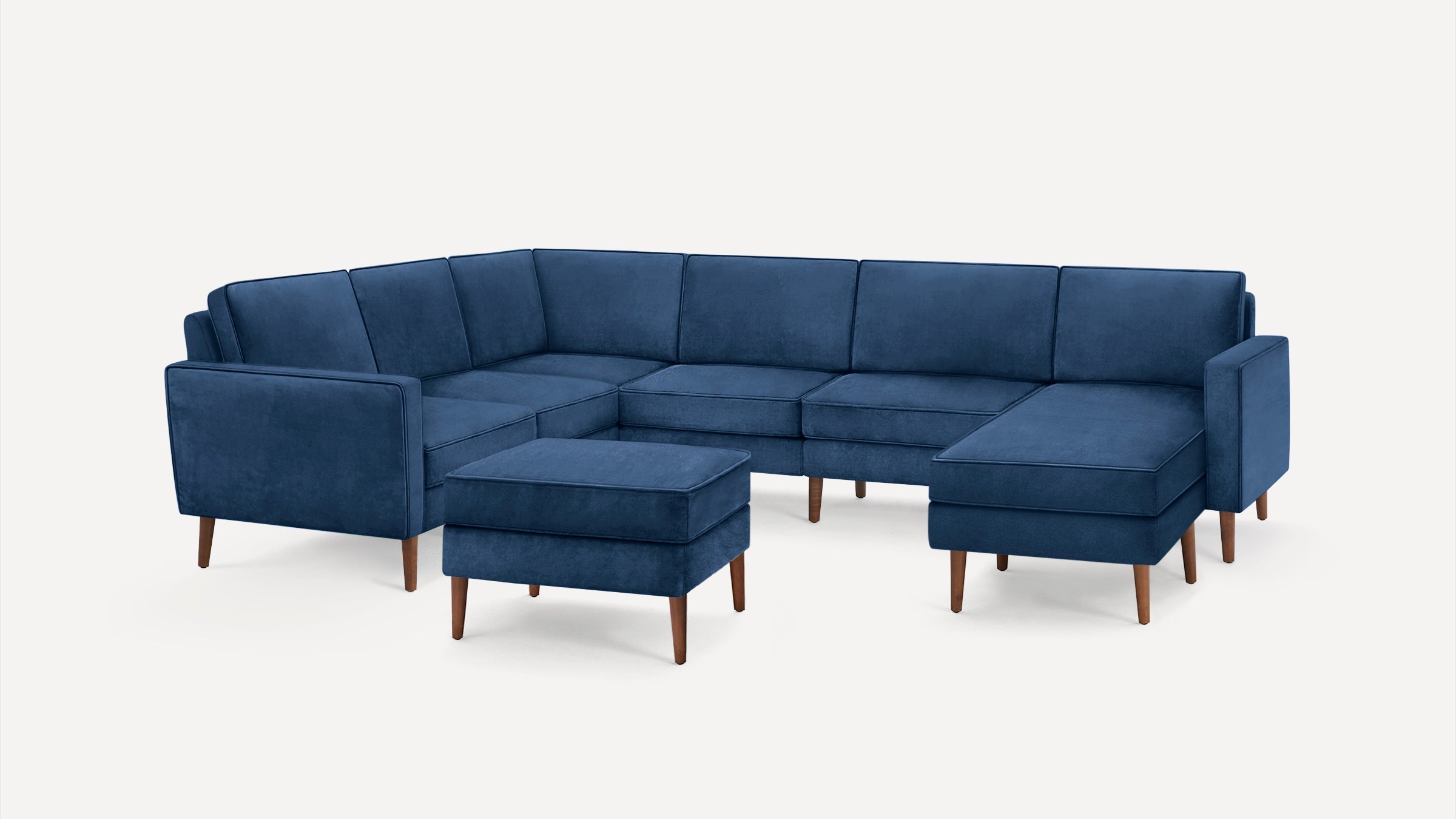 Modern navy blue L-shaped sectional sofa with wooden legs and matching ottoman on white background.