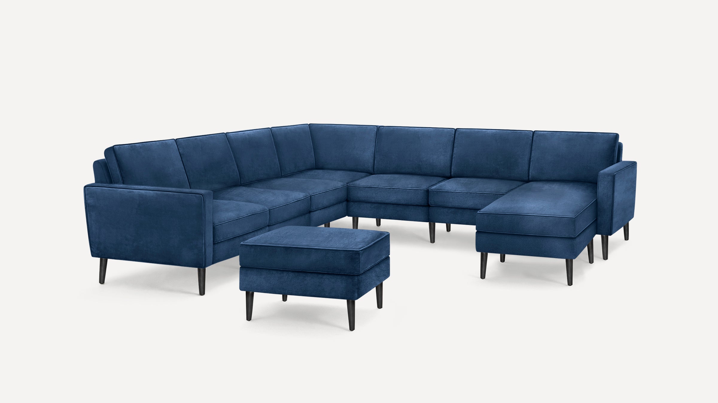 Modern navy blue velvet upholstered sectional sofa with matching ottoman, featuring clean lines and black tapered wooden legs.