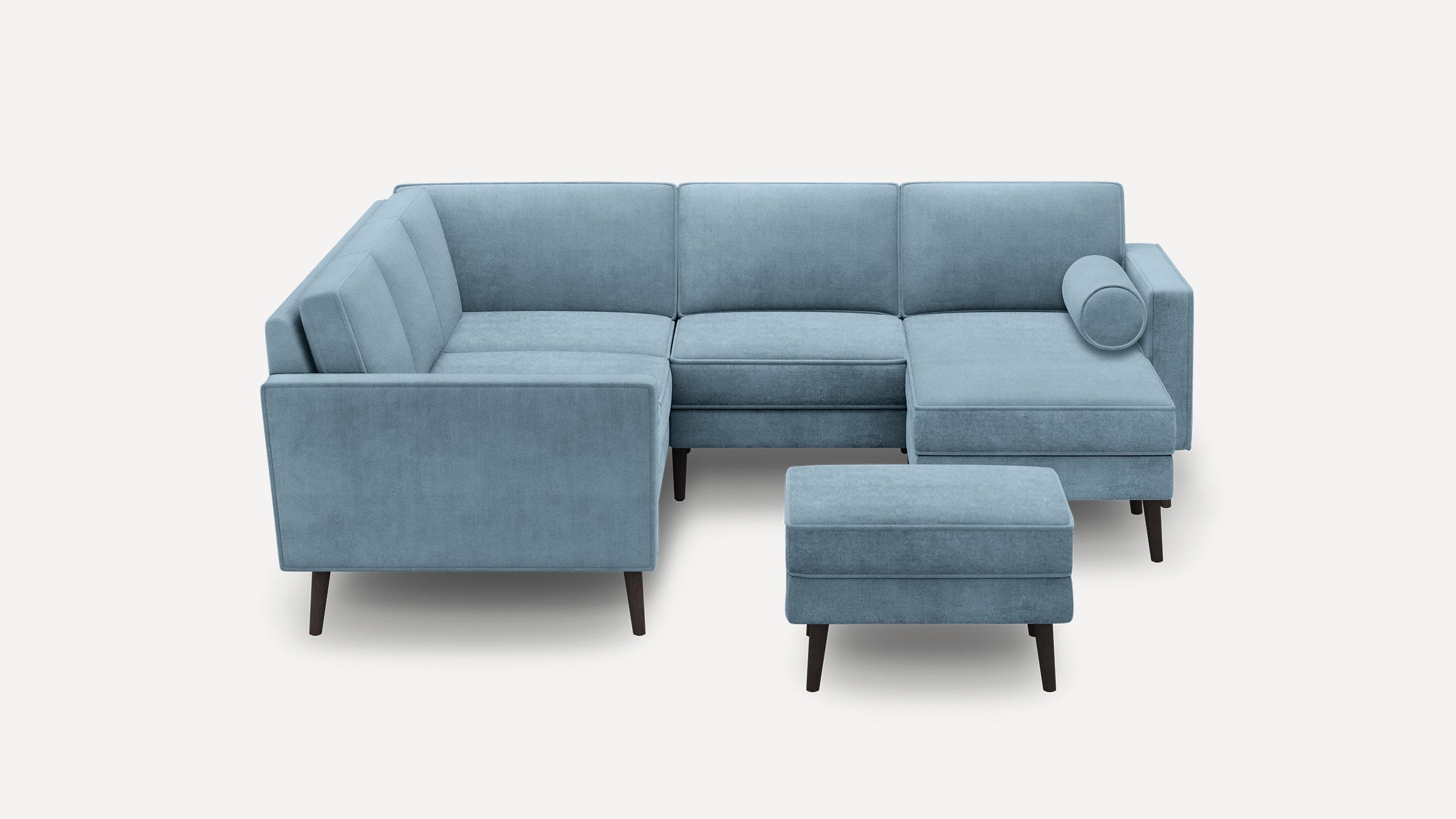 Light blue velvet L-shaped sectional sofa with tapered dark wooden legs and matching ottoman on neutral background.