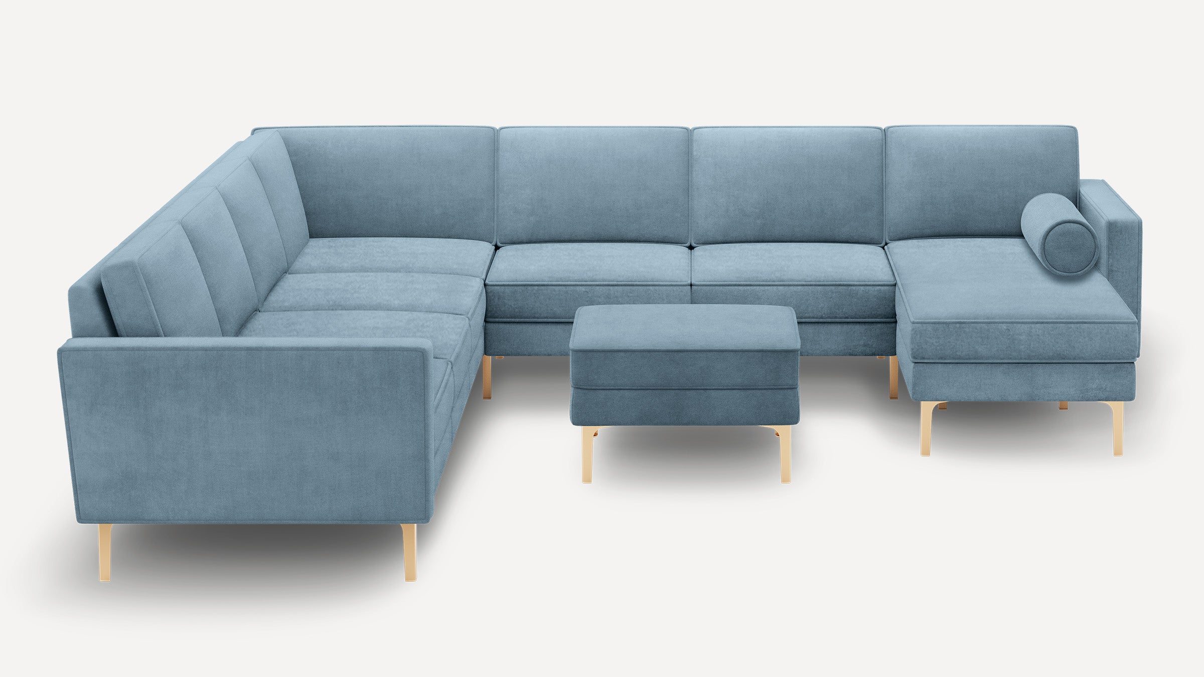 Modern light blue velvet sectional sofa with gold tapered legs and matching ottoman, featuring a cylindrical bolster pillow.