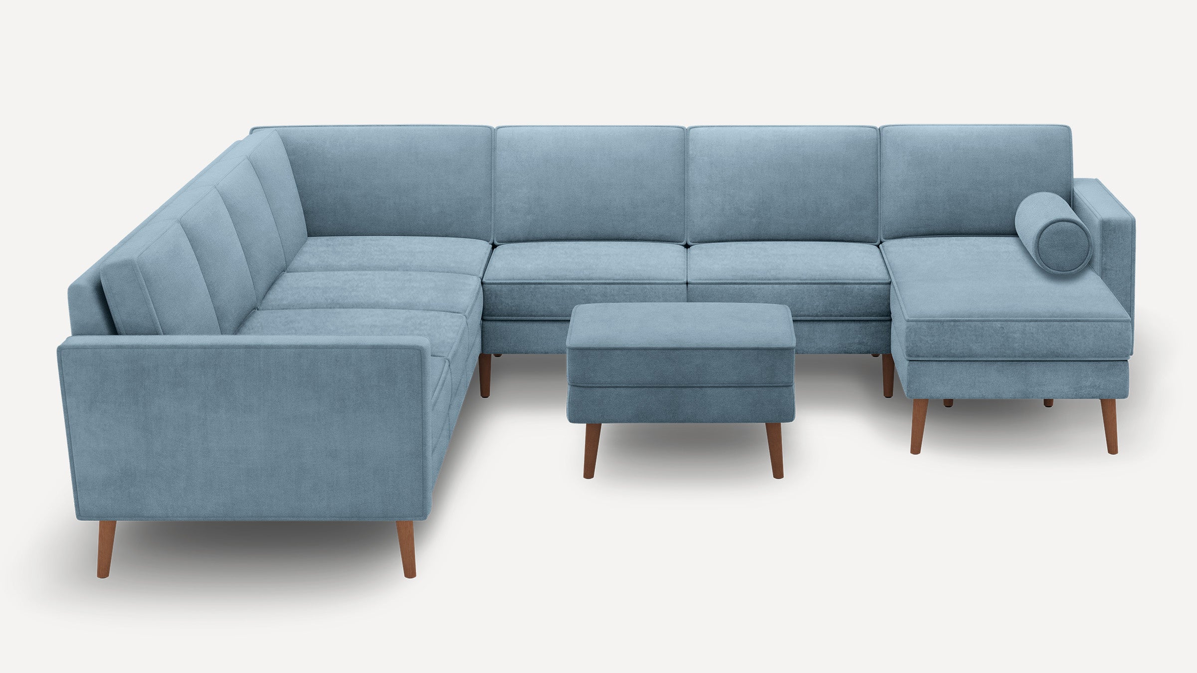 Light blue L-shaped sectional sofa with wooden legs, tufted cushions, and matching ottoman against a plain white background.