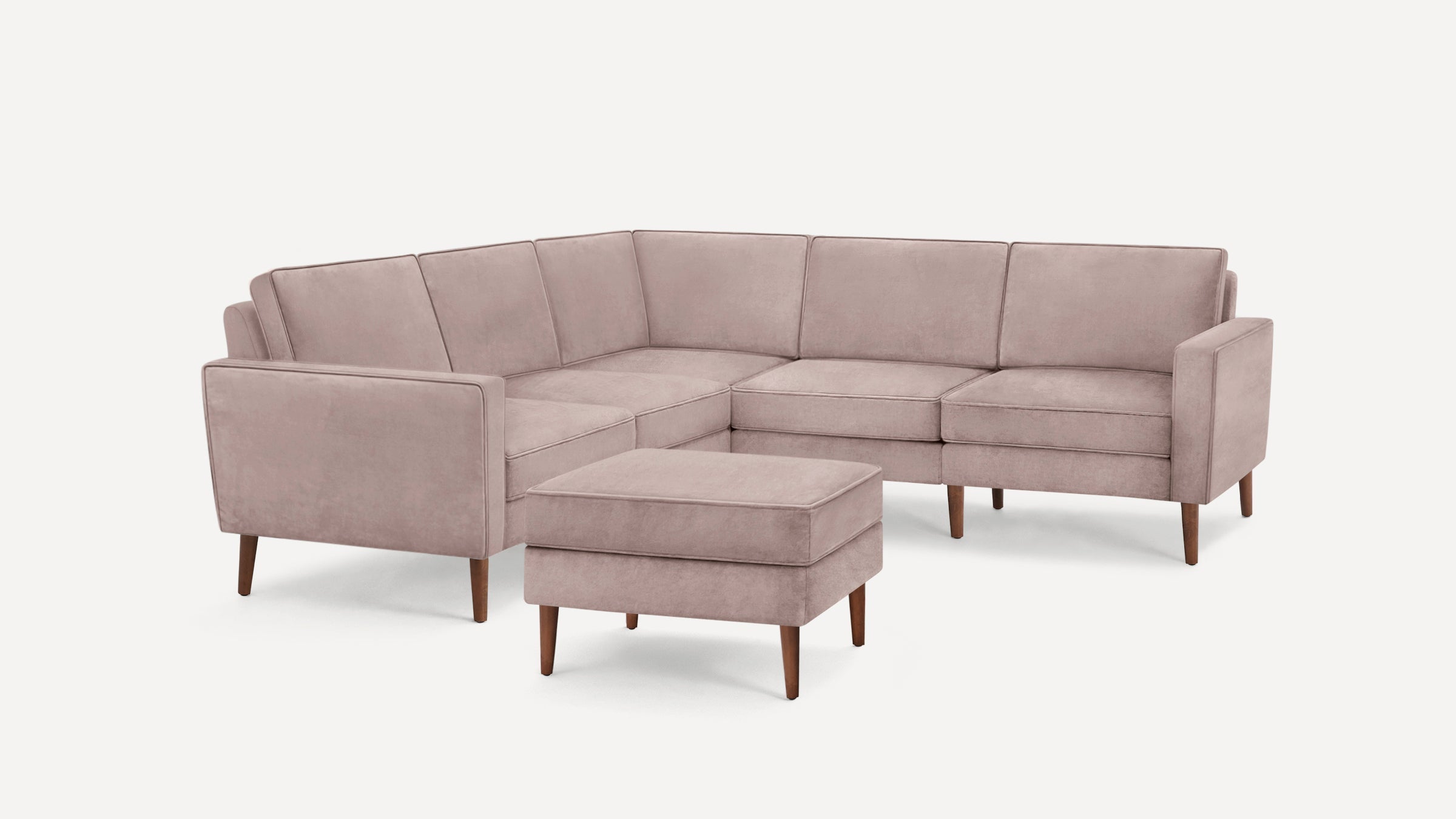Light mauve L-shaped sectional sofa with clean lines, square cushions, and matching rectangular ottoman on wooden legs.