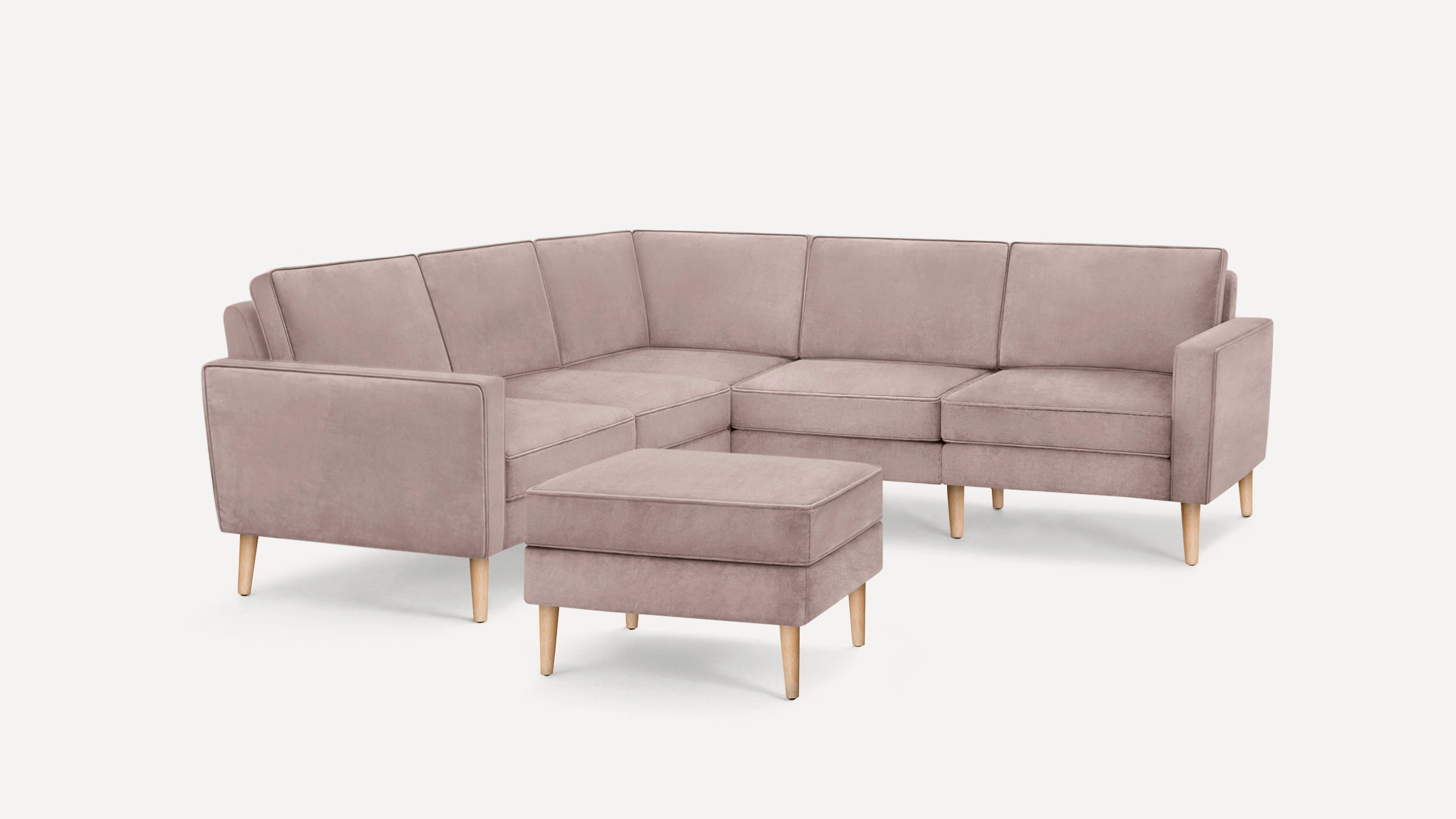 Light mauve fabric sectional sofa with wooden tapered legs and matching ottoman on white background.